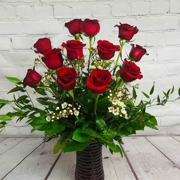 Red roses arranged in a dark ribbed vase with white filler flowers