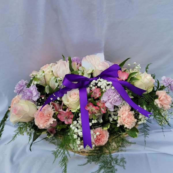 Pastel rose and carnation arrangement with a purple ribbon in a basket