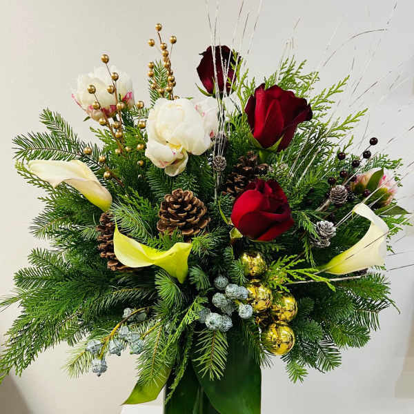 Tall holiday arrangement with red roses, white blooms, calla lilies, evergreens, pinecones and gold ornaments in a green vase
