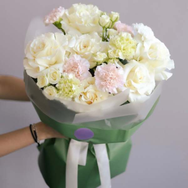 Bouquet of white roses and pale pink carnations wrapped in green paper
