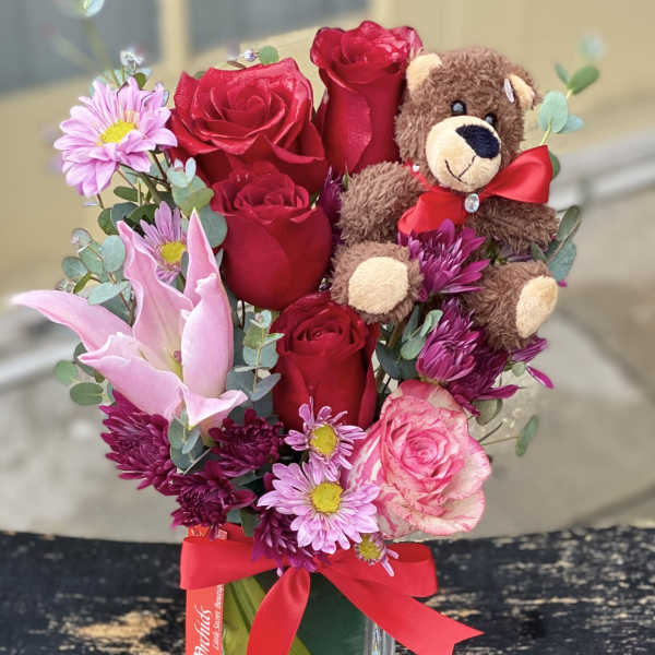 Bouquet of red roses and pink flowers with a teddy bear in a glass vase