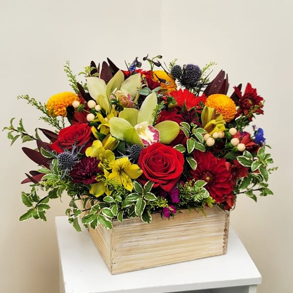 Mixed floral arrangement in a wooden box with red roses and green orchids