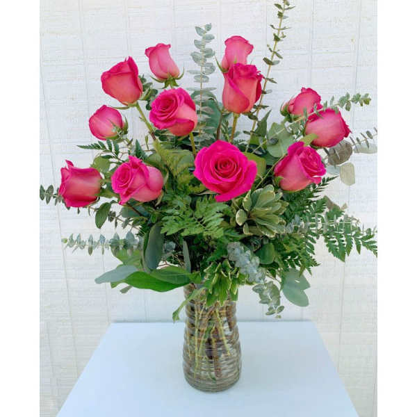 Pink roses arranged in a clear glass vase with eucalyptus and fern foliage.