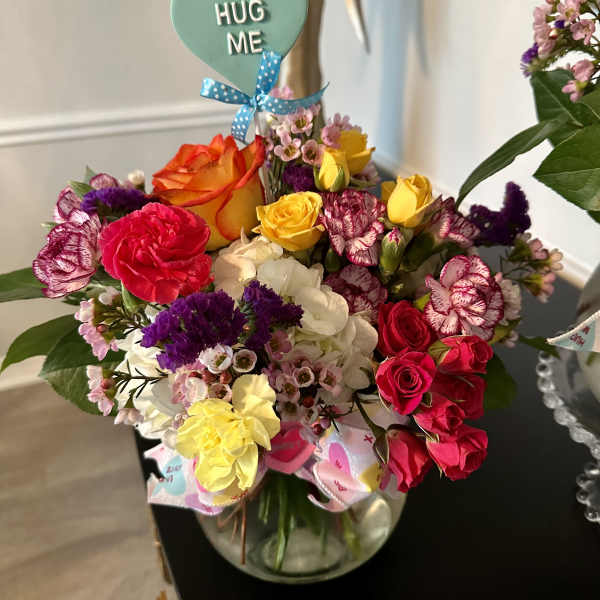 Mixed bouquet in a glass vase with a "HUG ME" heart pick