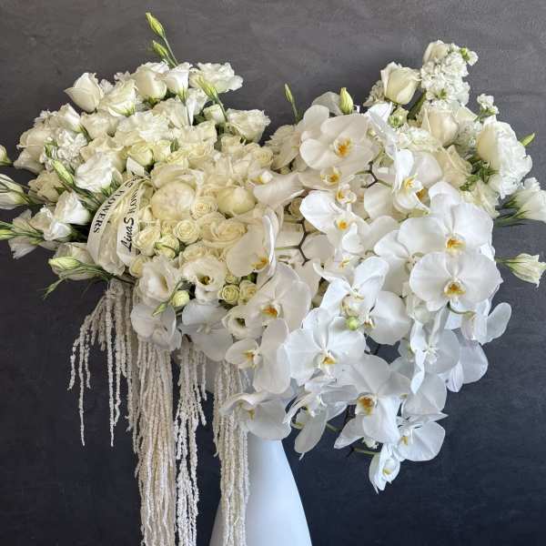 Large white floral arrangement in a tall vase with cascading orchids
