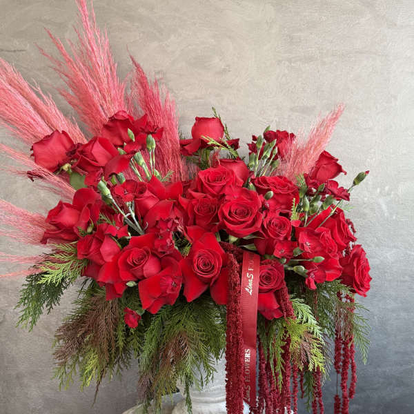 Large red rose arrangement with pink feathery accents in a white pedestal vase