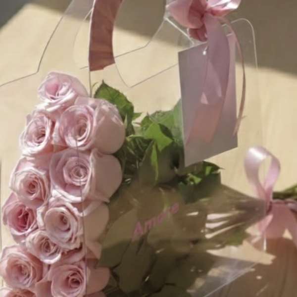 Pink roses in a clear gift box with a ribbon handle