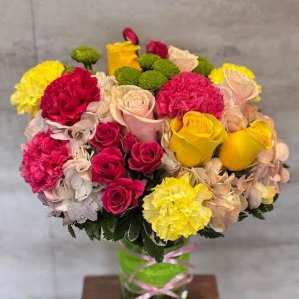 Mixed bouquet of roses, carnations, and hydrangeas in a glass vase