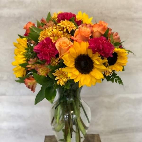 Mixed bouquet with sunflowers, roses, and mums in a clear glass vase