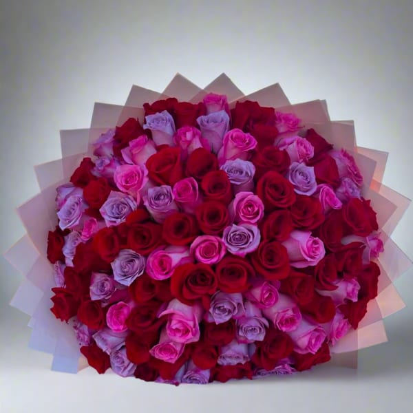Large bouquet of red, pink, and lavender roses wrapped in pale paper