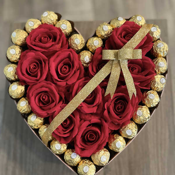 Heart-shaped box with red roses and gold-wrapped chocolates tied with a glitter ribbon