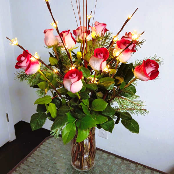 Tall vase arrangement of red and white roses with lit decorative branches