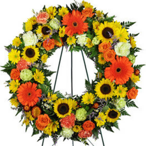 Circular wreath of sunflowers, orange gerberas, and roses on a stand
