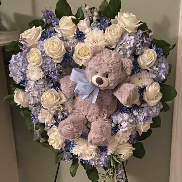 Heart-shaped floral wreath with a teddy bear and blue ribbon on an easel