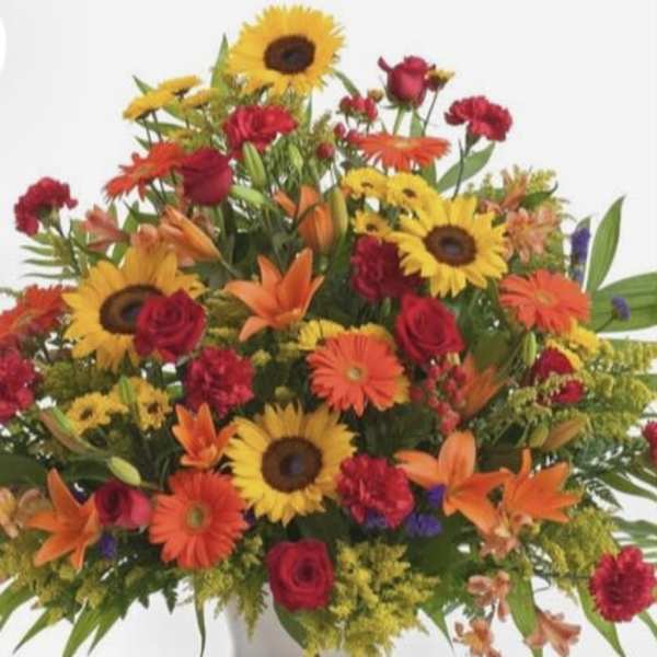 Colorful mixed bouquet with sunflowers, roses, gerbera daisies, and lilies in a white vase