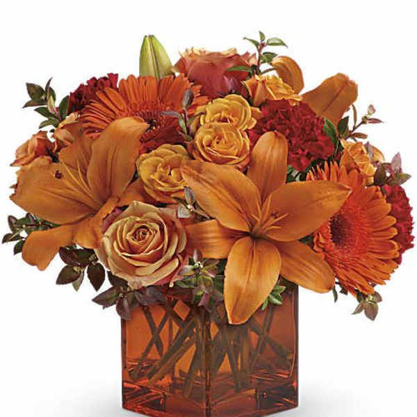 Orange and red flower arrangement in a square glass vase