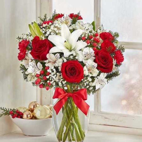 Red roses and white lilies in a clear glass vase with a red ribbon