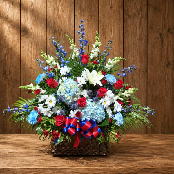 Large mixed flower arrangement in a wicker basket with red, white, and blue blooms