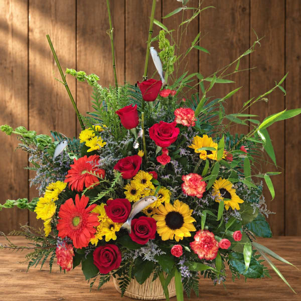 Large mixed bouquet of red roses, sunflowers, and gerbera daisies in a basket
