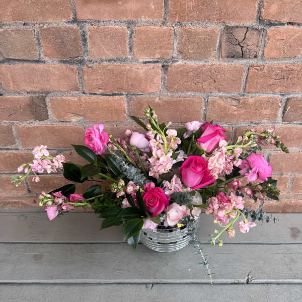 Pink roses and mixed blooms arranged in a mirrored vase.
