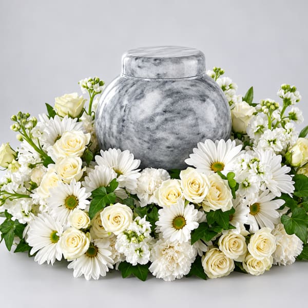 White roses and daisies arranged around a gray urn