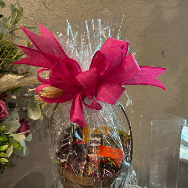 Basket of assorted chocolates wrapped in clear cellophane with a bright pink bow