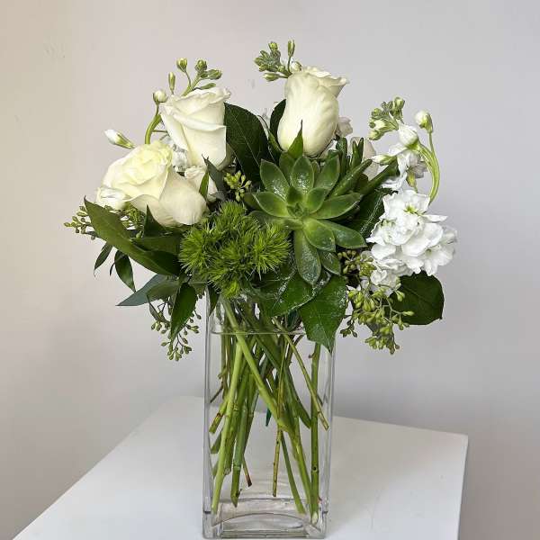 White roses and green succulents in a clear glass vase