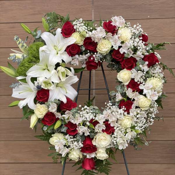 Heart-shaped floral wreath with red and white roses and lilies on a stand