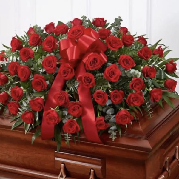 Large red rose casket spray with a red ribbon on a wooden casket