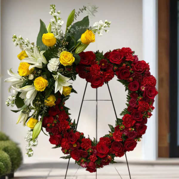 Heart-shaped floral wreath on a stand with red and yellow roses and white lilies
