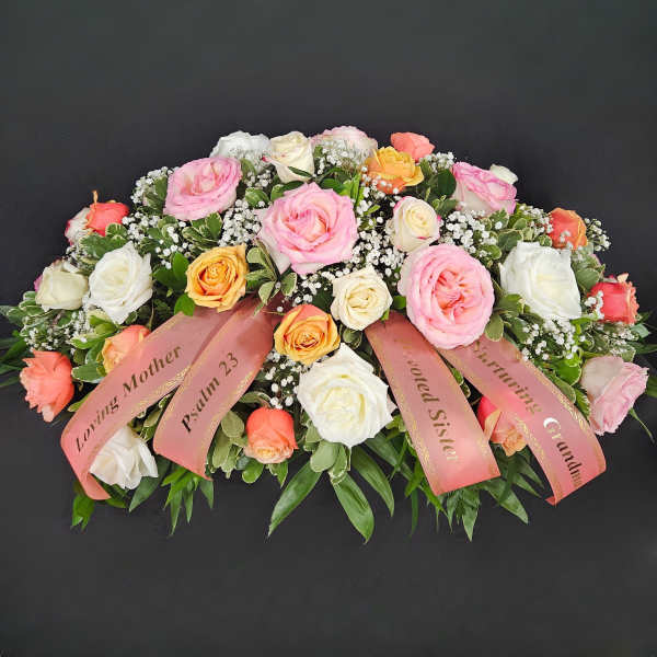 Large pink, white, and peach rose arrangement with ribbons on a dark background