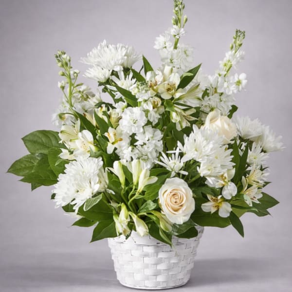 White floral arrangement in a white woven basket with green foliage
