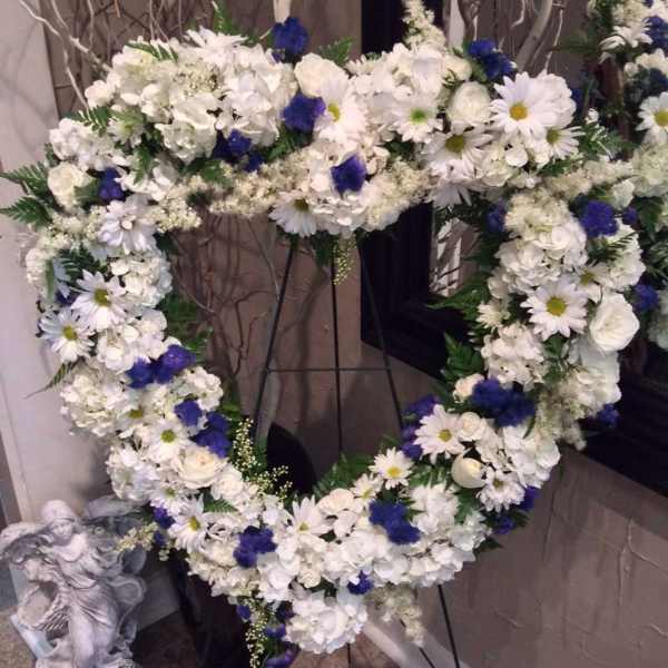 Heart-shaped floral wreath of white and blue flowers on a stand