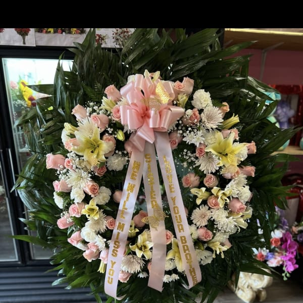 Large pink and white funeral wreath on a stand with ribbons