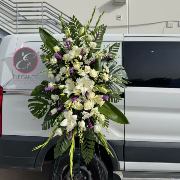 Tall white floral standing spray with purple accents on a metal easel