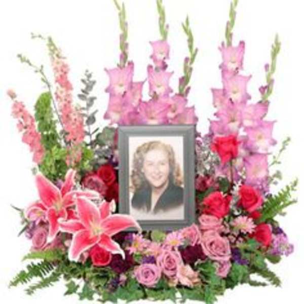 Pink and red floral memorial arrangement with a framed portrait in the center