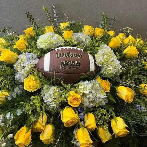 Yellow roses and pale hydrangeas arranged around a football centerpiece