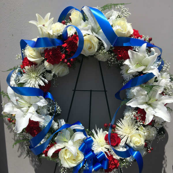 Circular wreath of white lilies, roses, and red carnations with blue ribbon