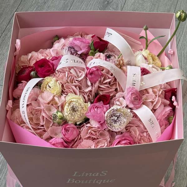 Pink bouquet in a box with roses and hydrangeas tied with white ribbons