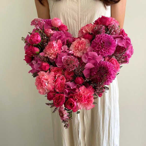 Heart-shaped bouquet of pink flowers held by a person in a white dress