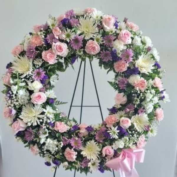 Pastel floral wreath on a black stand with a pink ribbon