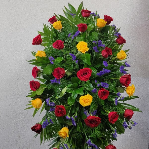 Large standing arrangement of red and yellow roses with purple filler flowers