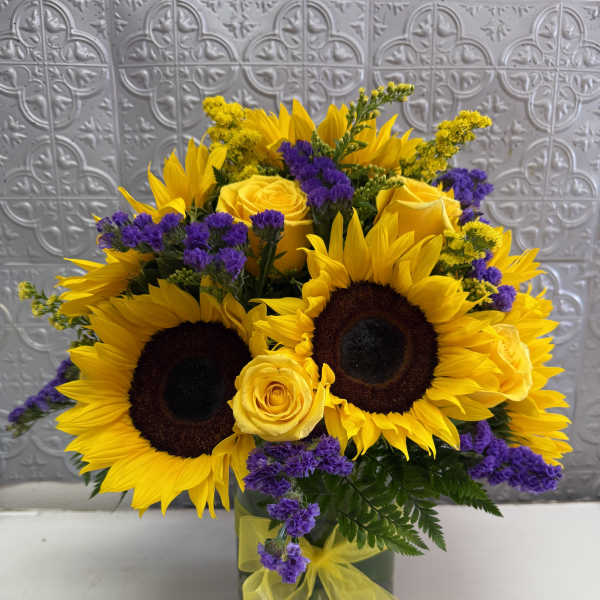 Sunflower and yellow rose bouquet in a glass vase with purple accents