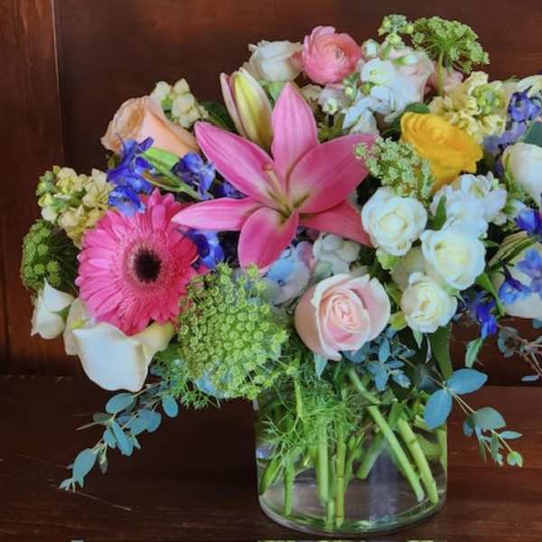 Mixed bouquet of pink, white, yellow, and blue flowers in a glass vase