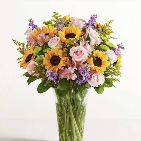Bouquet of sunflowers, pink roses, and purple flowers in a clear glass vase