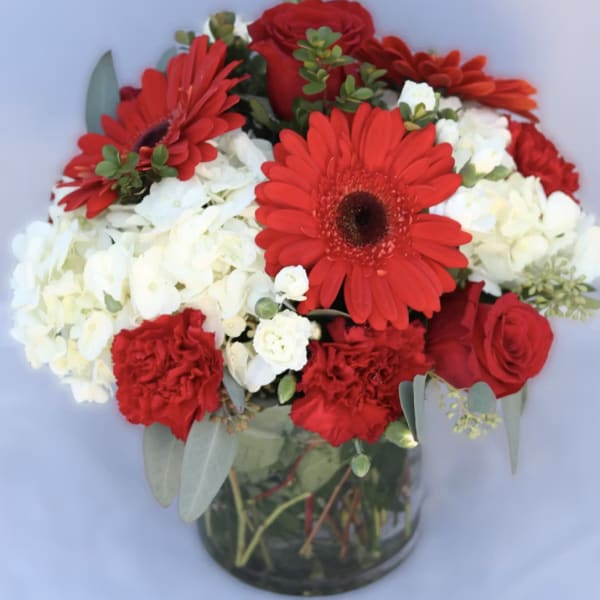 Red gerbera daisies, roses, and white hydrangeas in a glass vase