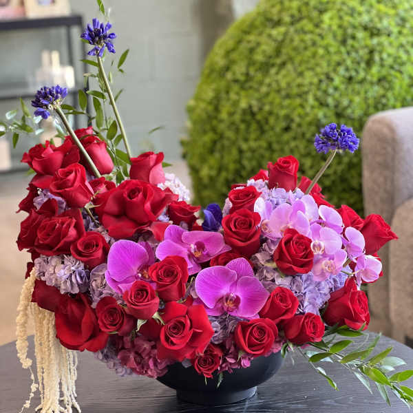 Red roses and pink orchids arranged in a black bowl vase