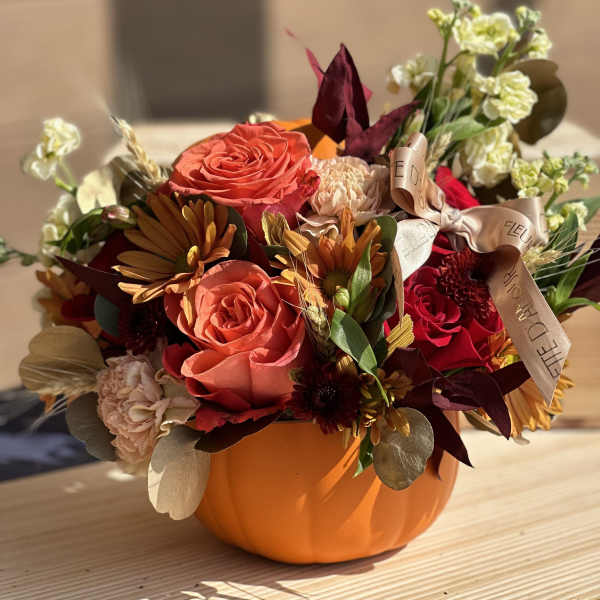 Orange pumpkin-shaped container with mixed autumn flowers and ribbon