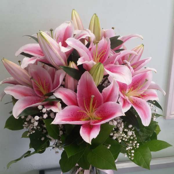 Pink lilies arranged in a clear glass vase with baby's breath