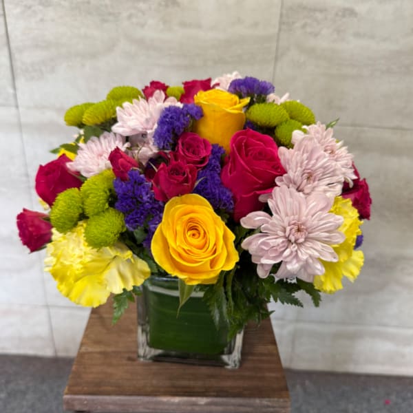 Colorful bouquet of roses and chrysanthemums in a square glass vase